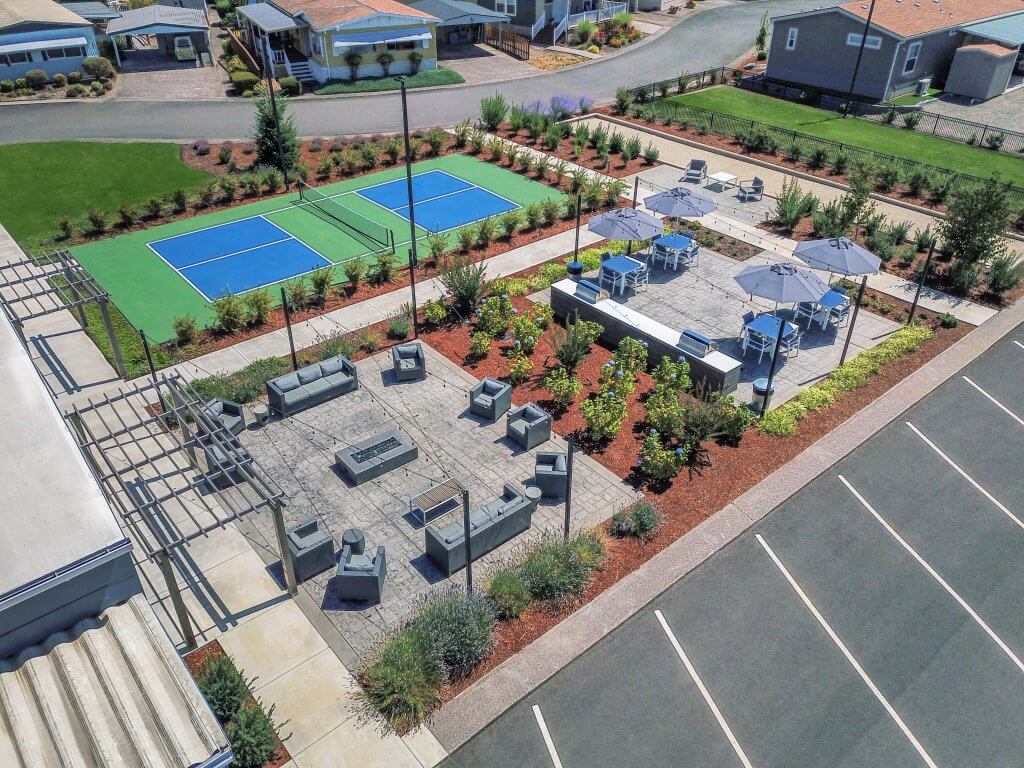 Aerial view of a landscaped outdoor area with pickleball courts, fire pits, patio seating, and nearby homes in salem oregon
