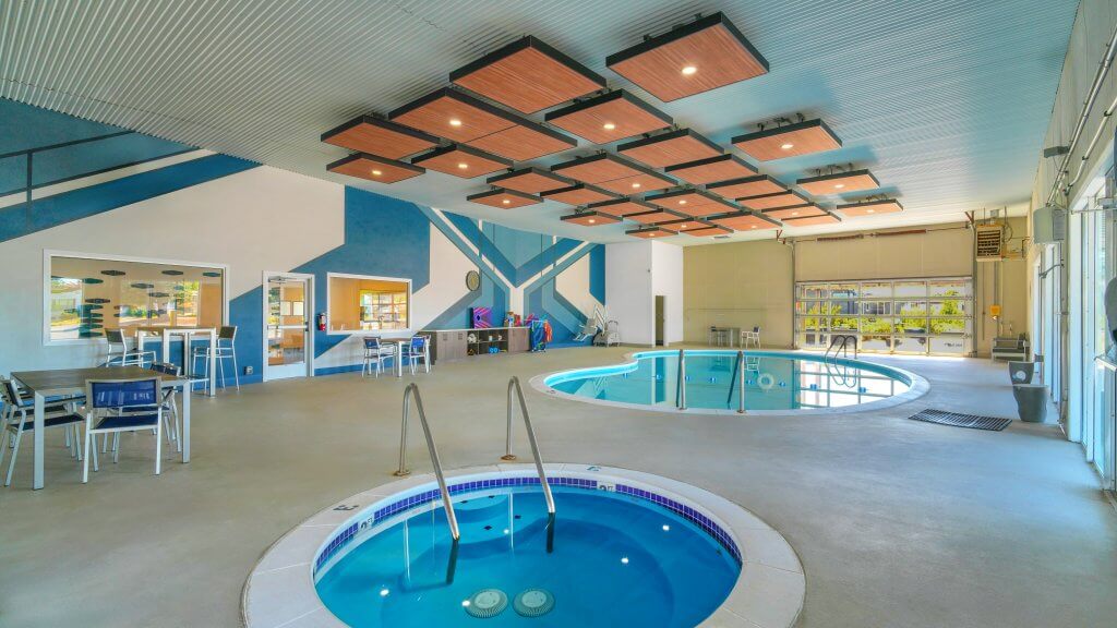Bright indoor pool area with a round hot tub, large pool, modern decor, and tables with chairs in salem oregon