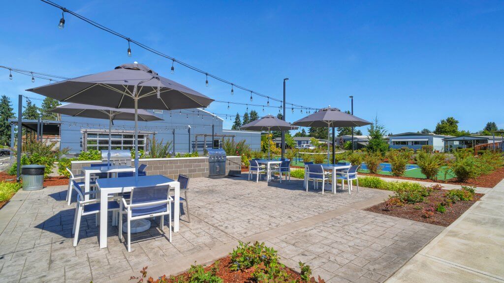 Outdoor patio with tables, chairs, umbrellas, string lights, and a grill area surrounded by plants and pathways in salem oregon
